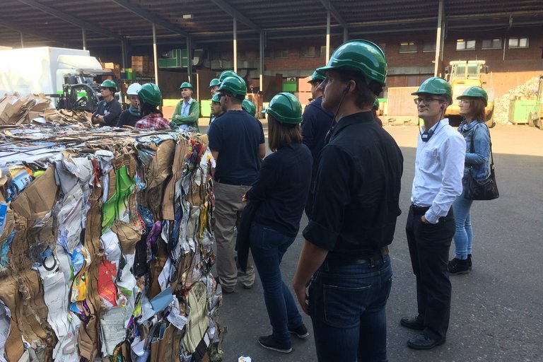 Teilnehmende stehen auf einem Recyclinghof vor gepressten Ballen